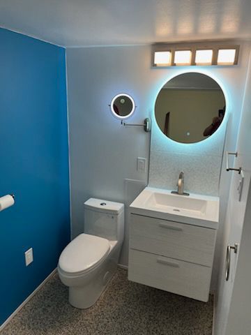 Modern bathroom with blue and white walls, floating vanity, round mirror with LED light, and toilet.