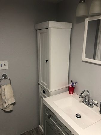 Bathroom with white storage cabinet, sink, mirror, and towel rack on gray wall.