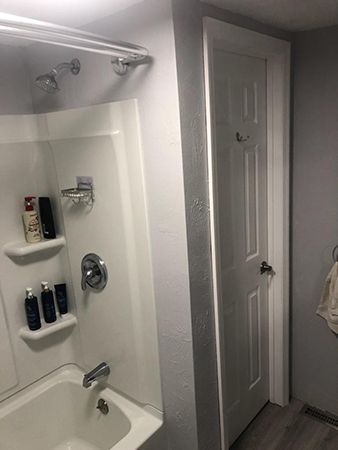 Bathroom interior with shower/tub, door with hooks, and gray walls.