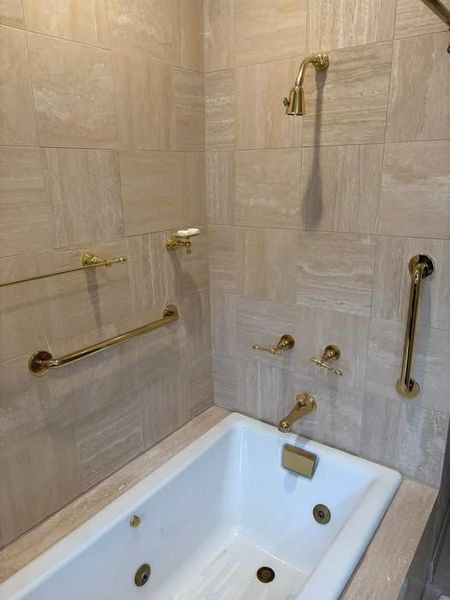 Bathroom with a white tub, gold fixtures, and beige tiled walls.