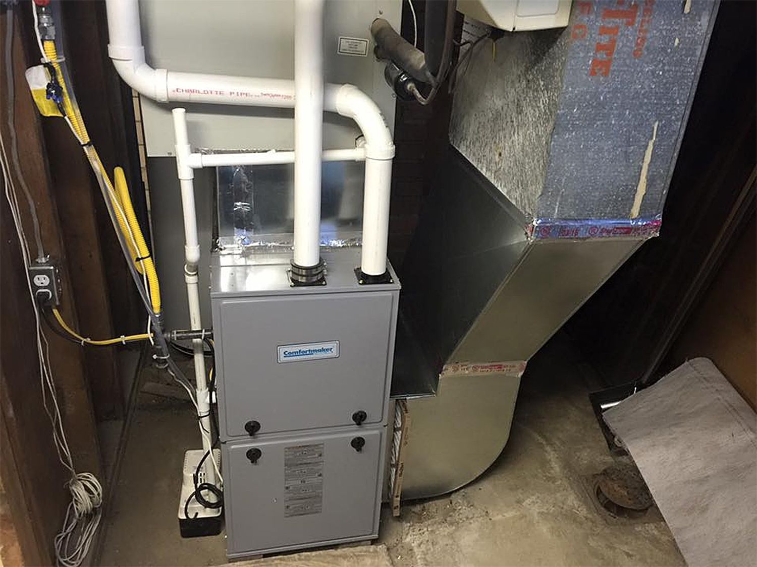 Gray furnace and ductwork in a basement setting, with white PVC pipes and electrical wiring visible.