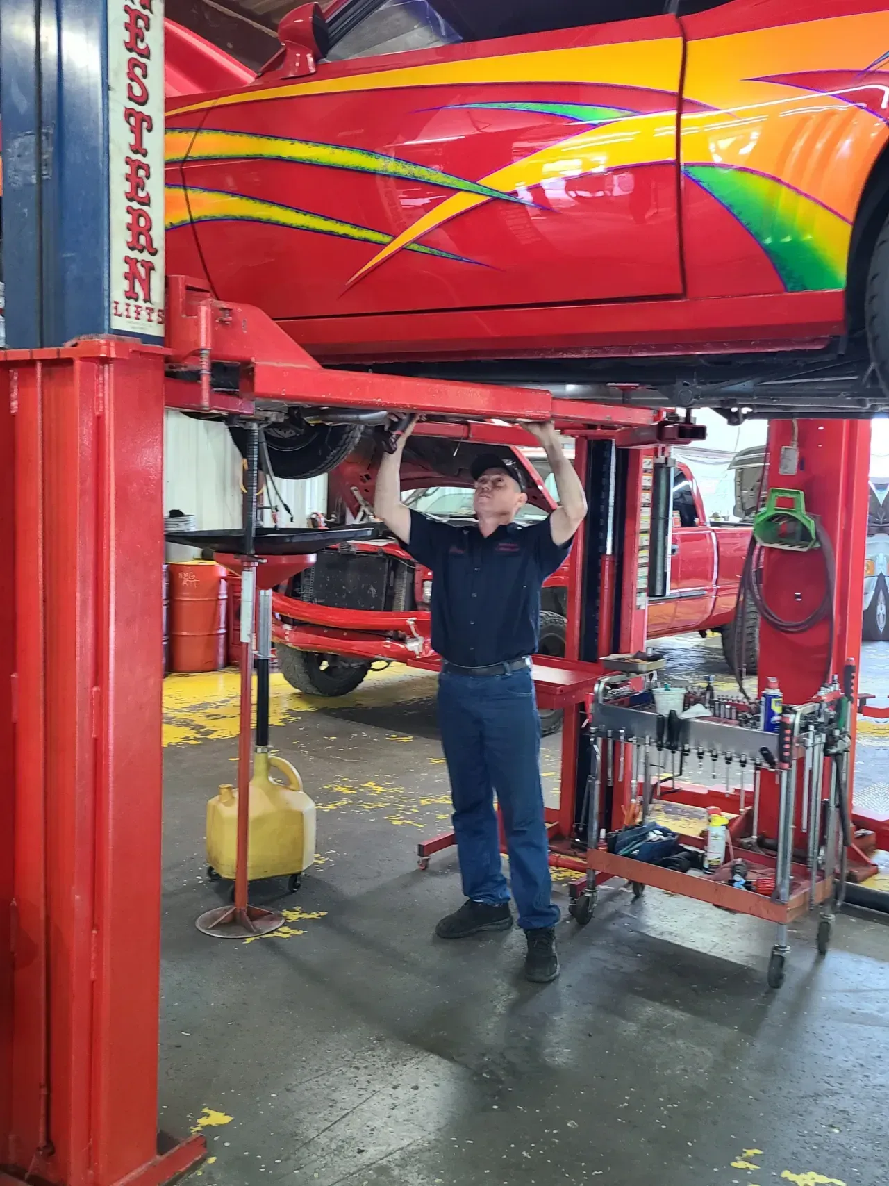 Mechanic standing under a red race car on a lift in an auto shop