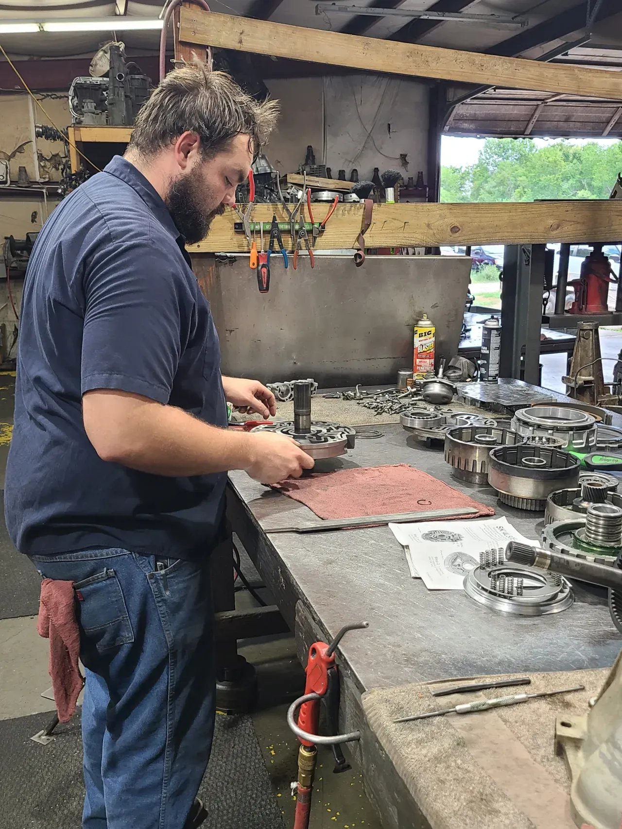 Man working at a cluttered workshop bench, focused on tools and metal parts.