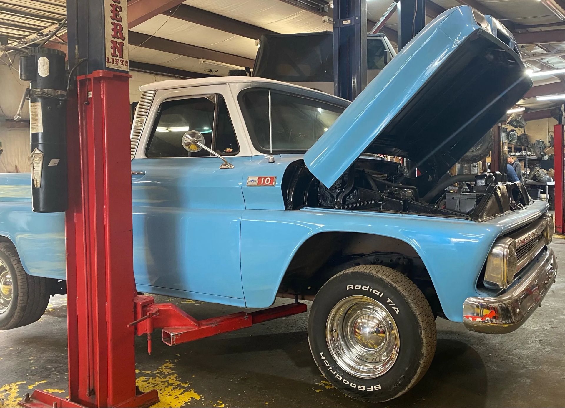 Light blue vintage pickup truck with hood open in a garage lift bay