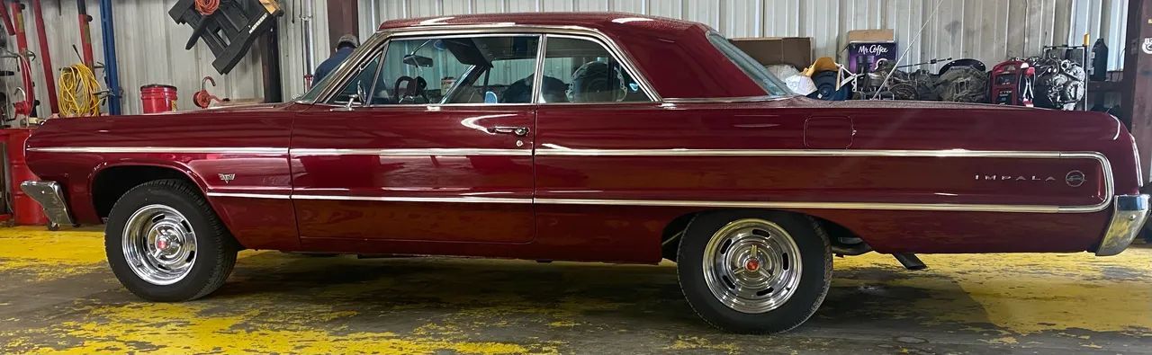 Classic maroon vintage car parked indoors in a garage or workshop, side view