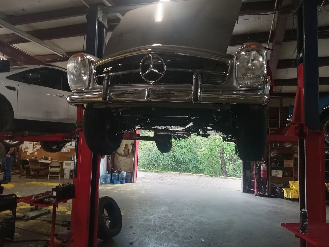 Classic Mercedes on a lift in an auto repair shop, front view with hood raised.