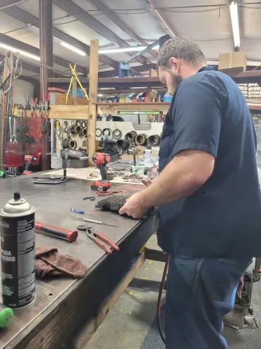 Person working at a cluttered metal shop workbench with tools and parts scattered around