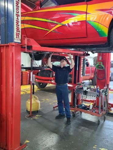 Mechanic inspecting a red car on a lift in an auto repair shop