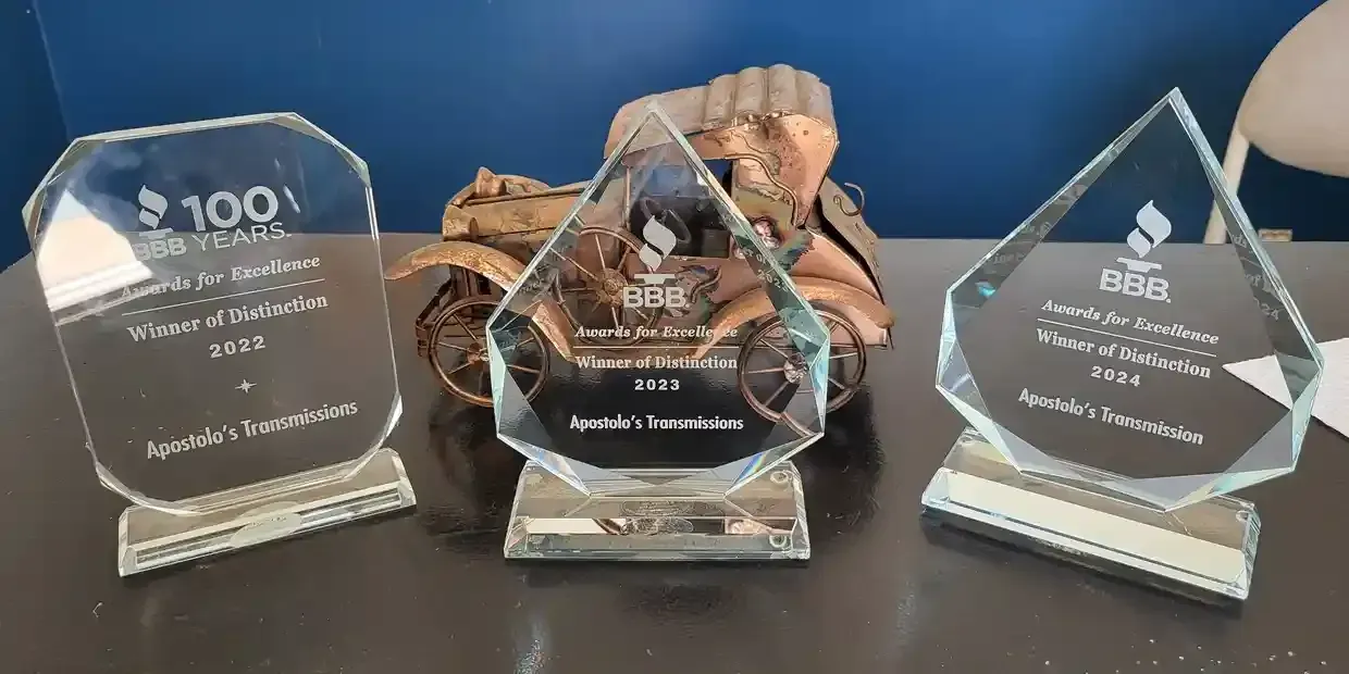 Three glass awards on a blue cloth, with gold-toned sculptural pieces in the center and flanking plaques.