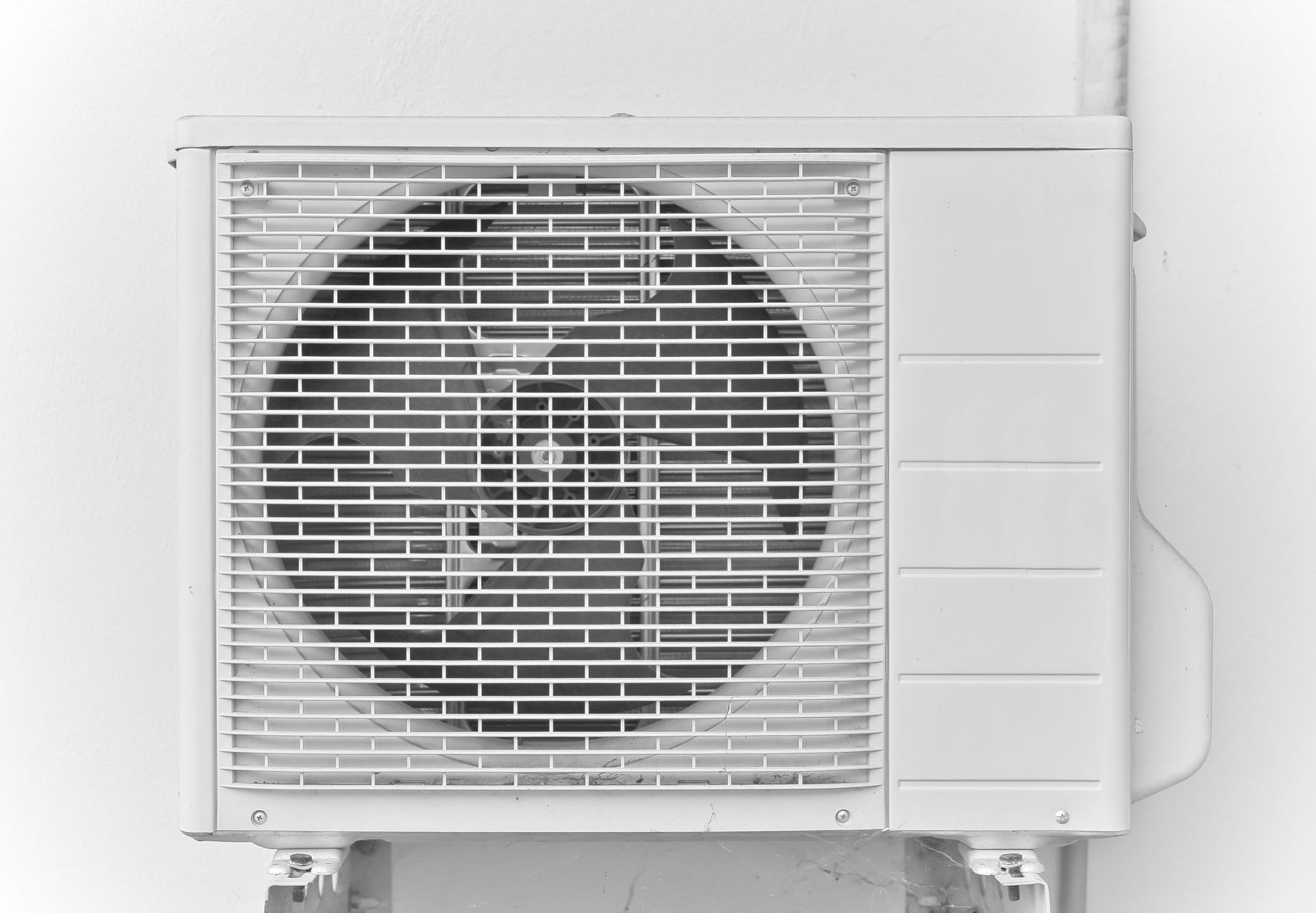 White air conditioning unit mounted on a white wall, with a protective metal grill over the fan.