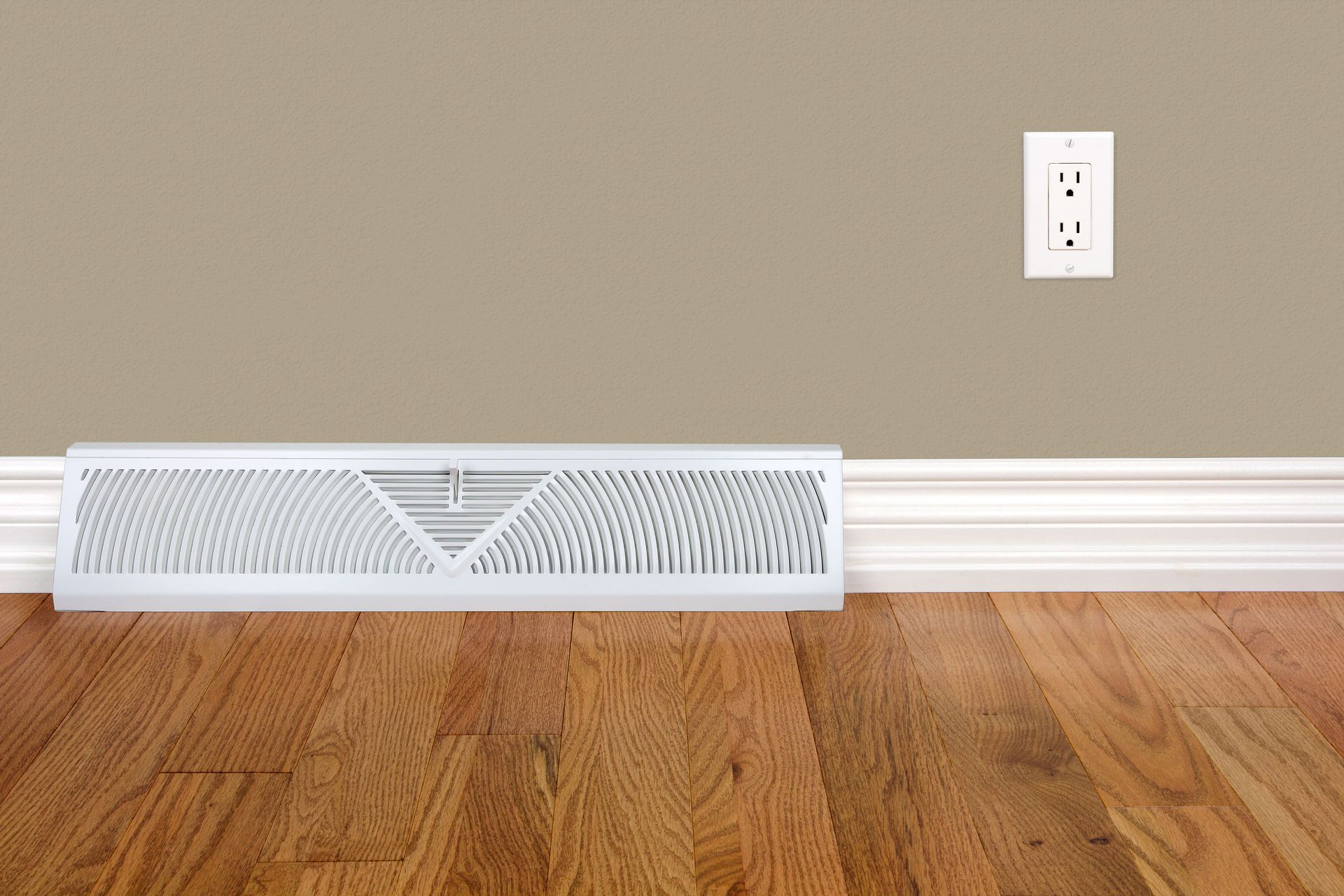 White baseboard heater against tan wall, electrical outlet above. Hardwood floor.
