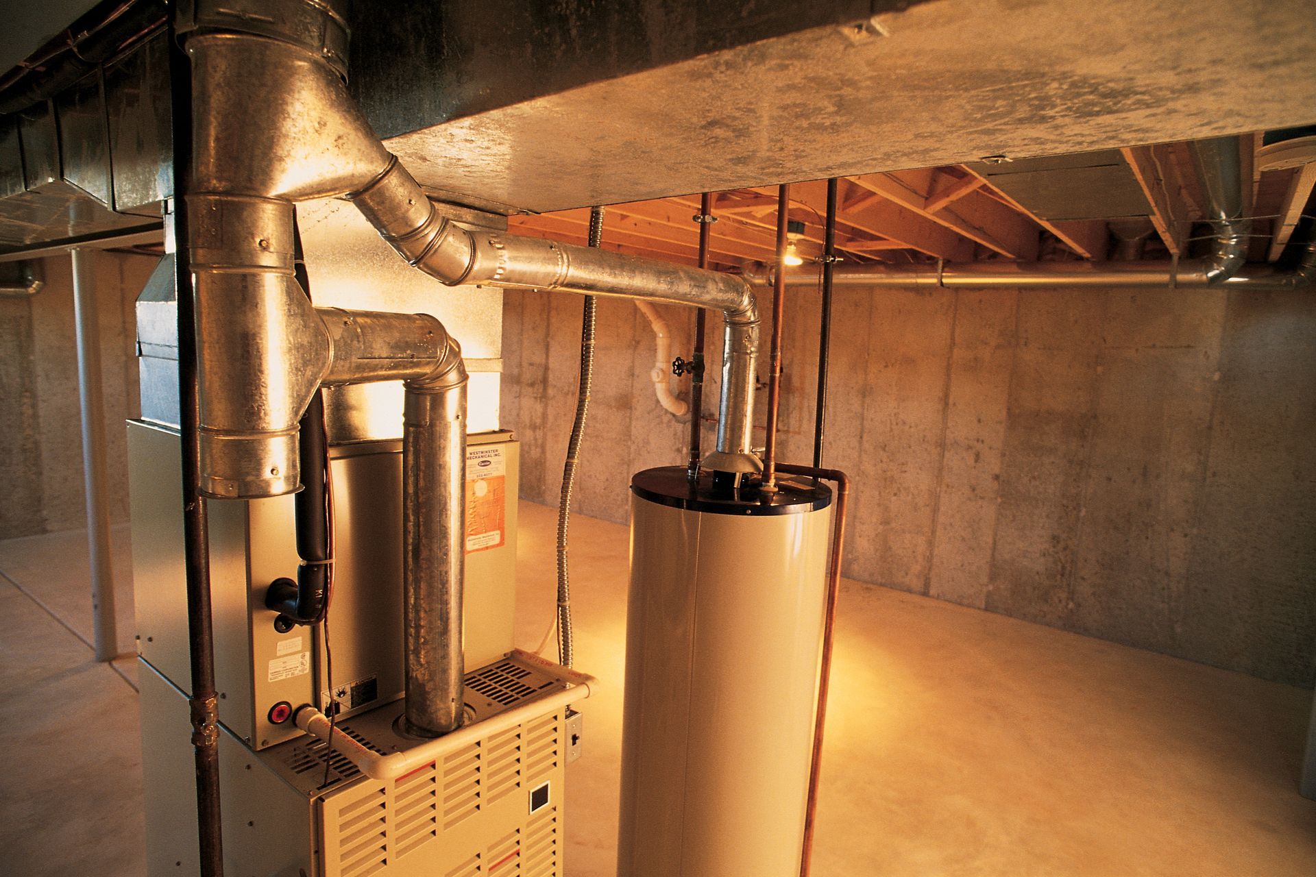Furnace and water heater in a basement with metal ductwork and concrete walls.