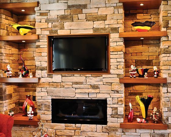 Stone fireplace wall with mounted TV and built-in shelves holding colorful decor