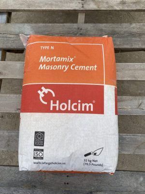 Bag of Holcim Mortamix masonry cement, orange and white, lying on a wooden bench