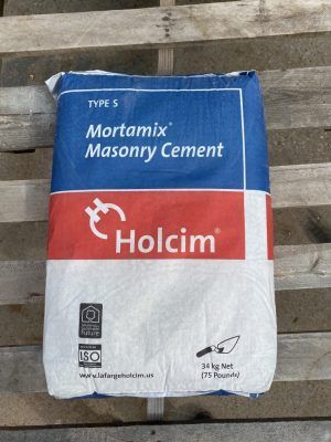 Holcim Mortamix masonry cement bag in blue, red, and white, standing on a wooden surface.