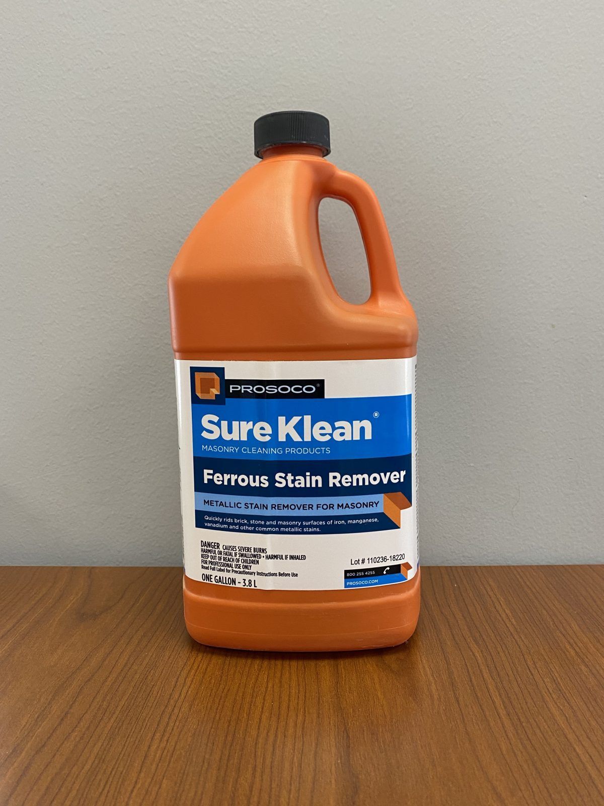 Orange bottle of Sure Klean Ferrous Stain Remover on a wooden table against a gray wall