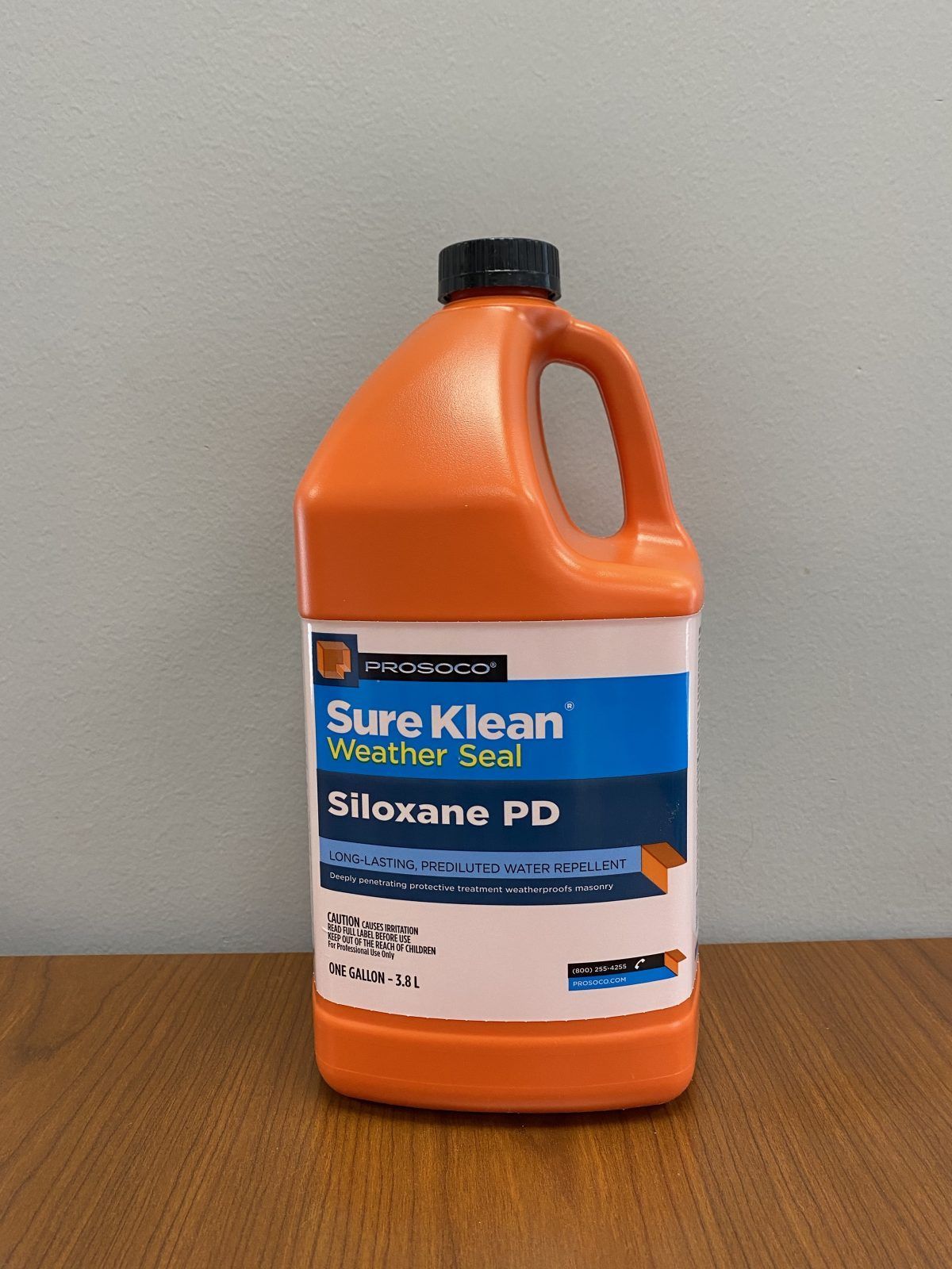Orange jug of Sure Kleen Silicone PD cleaner on a table against a gray wall