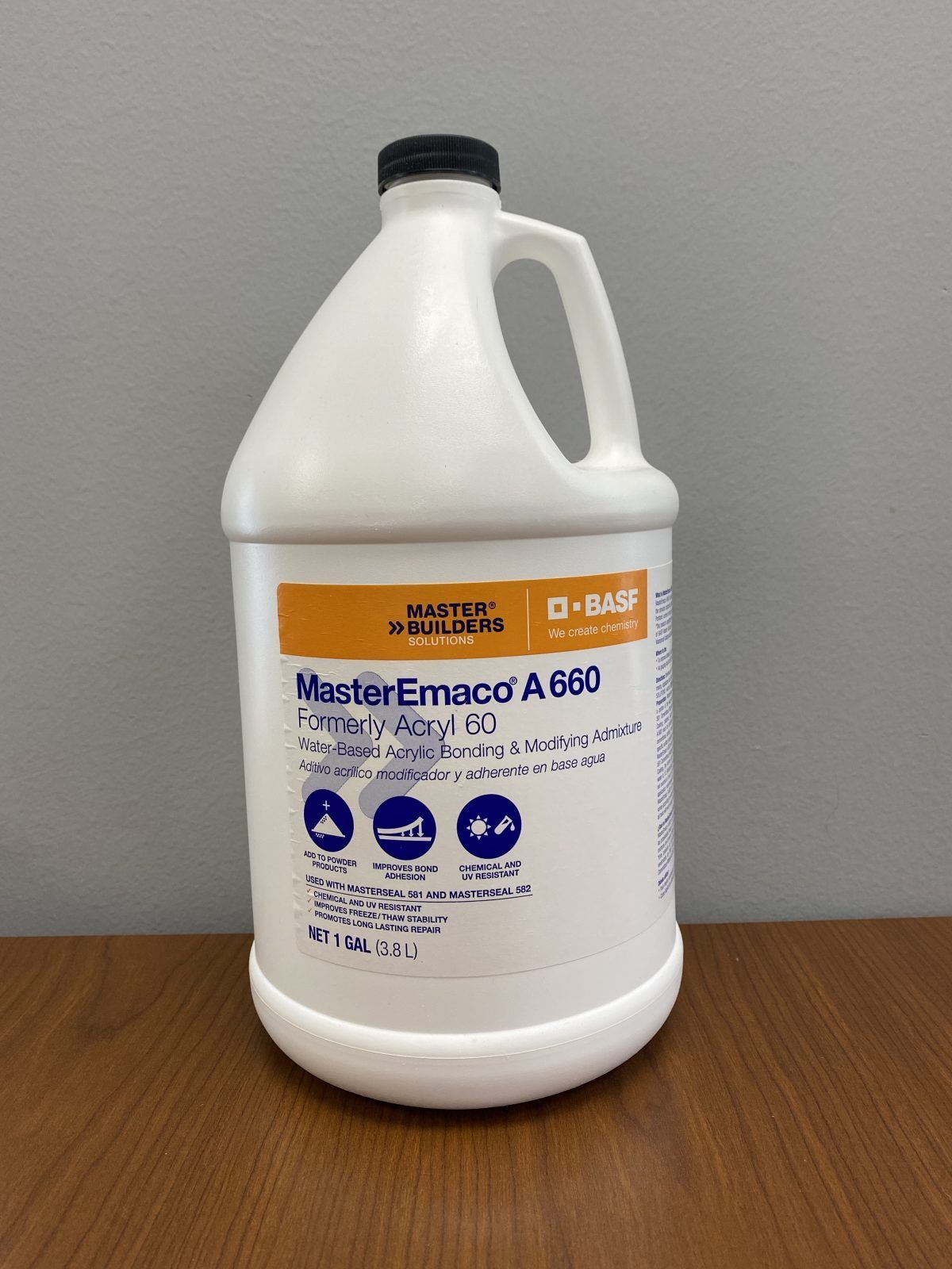 White plastic gallon jug of chemical cleaner with black cap on a wooden table against a gray wall