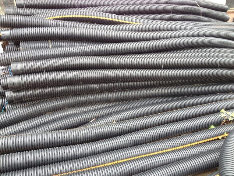 Stacked gray corrugated plastic pipes with yellow stripes, piled horizontally in a storage area