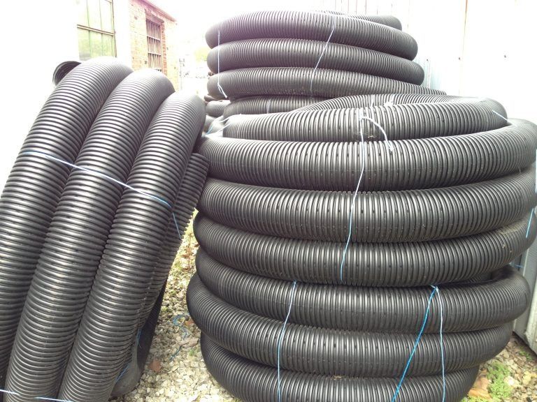 Stacks of large black corrugated pipes coiled outdoors near a building.