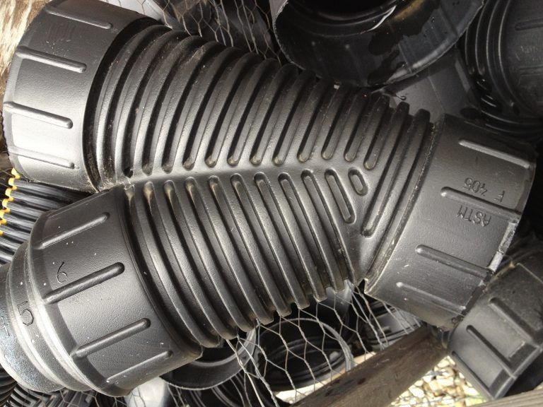 Black ribbed plastic pipes or ducts stacked in a pile inside a warehouse.