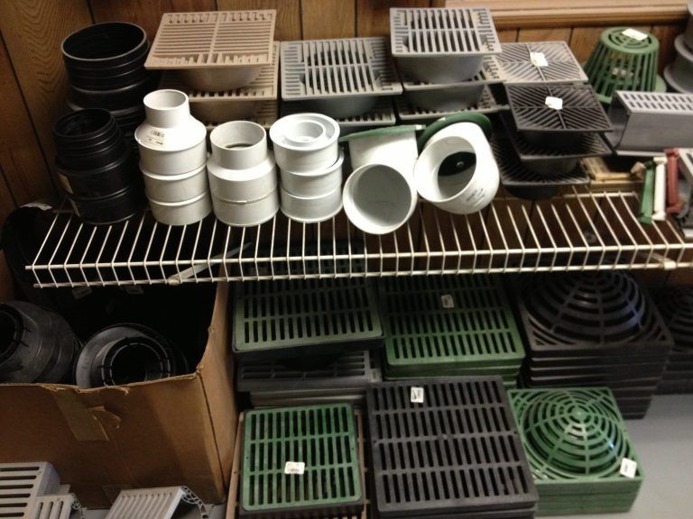 Shelves stacked with assorted plastic pipes, fittings, and grates in black, white, and green.
