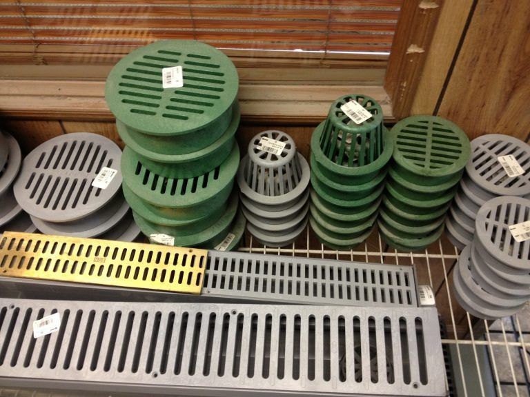 Assorted green and gray plastic drain grates stacked on a store shelf