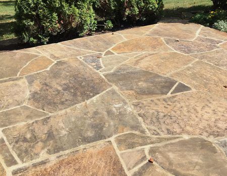 Stone patio with irregular tan and brown flagstones beside green shrubs