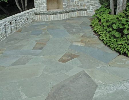 Stone patio walkway beside a stone wall and green shrubs in a garden