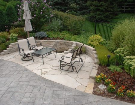 Stone patio seating area with metal chairs, glass table, umbrella, and landscaped garden border