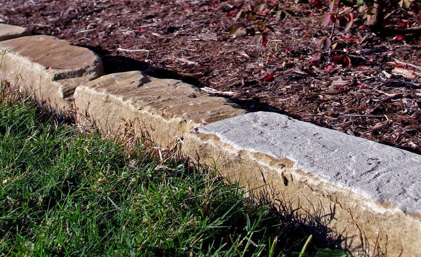 Stone garden edging beside grass and brown mulch in sunlight