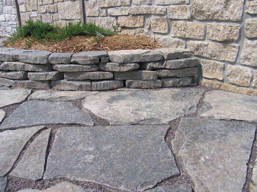 Stone patio with irregular flagstones and a small stacked stone planter against a wall.