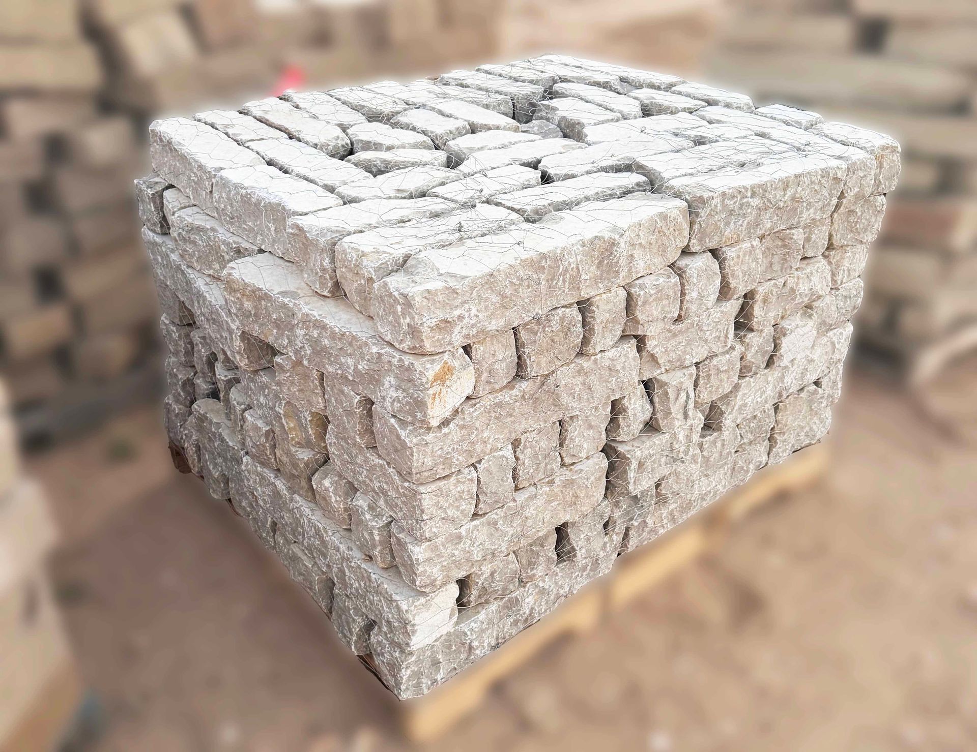 A rectangular pallet stacked with rows of rough, light-colored concrete bricks in an outdoor construction area.