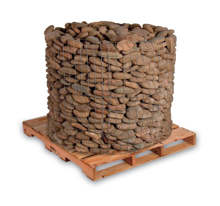 A large, cylindrical wire basket filled with rounded, brown river stones, sitting on a wooden shipping pallet.
