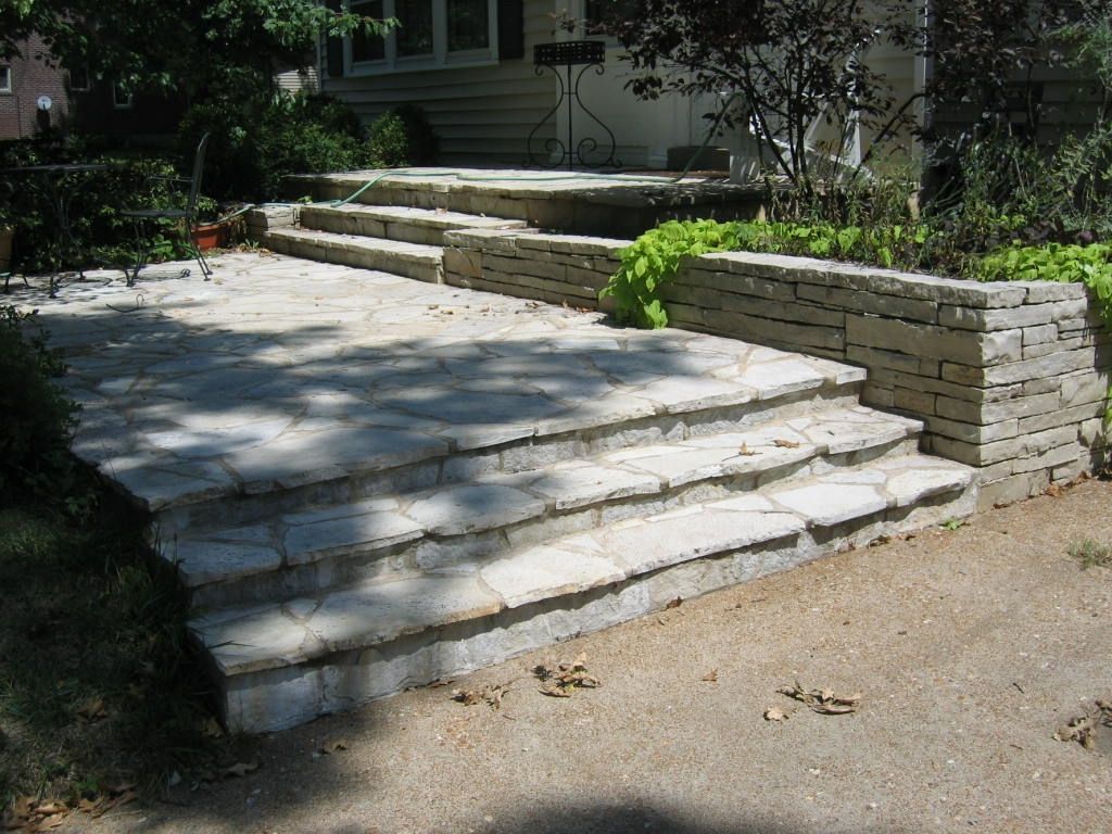 Flagstone patio with tiered stone steps leading to a raised stone wall and residential entrance.