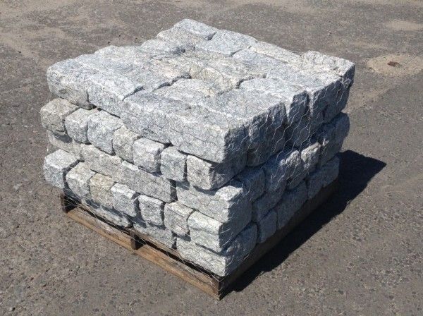 A square pallet of grey, rough-cut granite paving stones sits on a flat, paved surface.