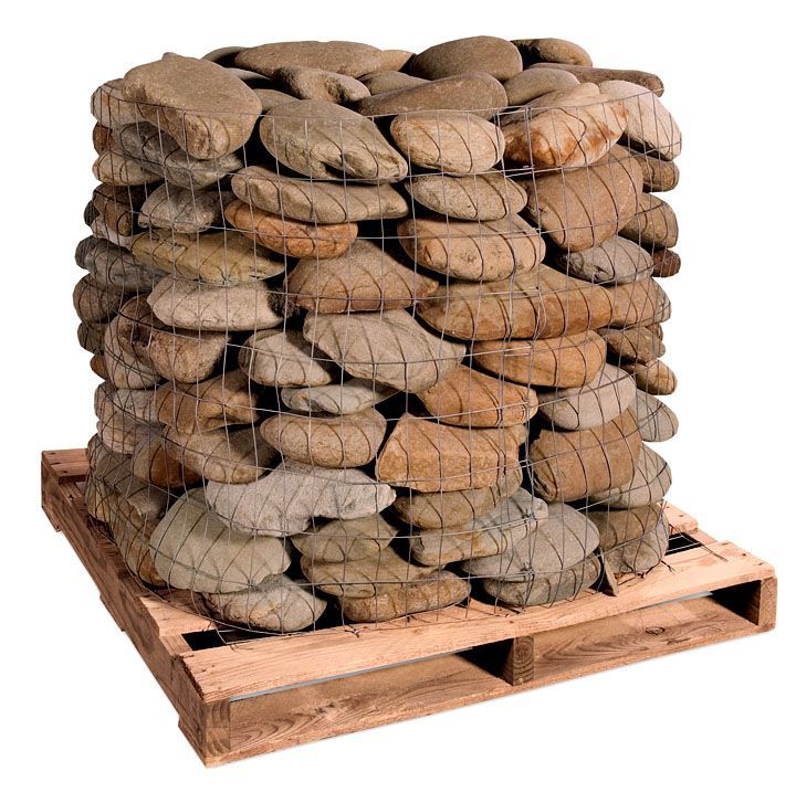 A large, square wire cage filled with flat, tan-colored stones, sitting on a wooden shipping pallet.