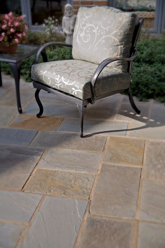 An outdoor patio chair with patterned cushions placed on a stone-paved floor next to a small side table.