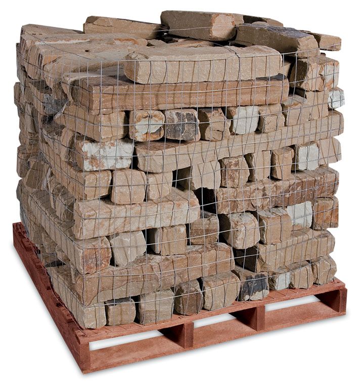 A wooden pallet piled with rustic, tan-colored rectangular stone blocks secured inside a wire mesh cage.