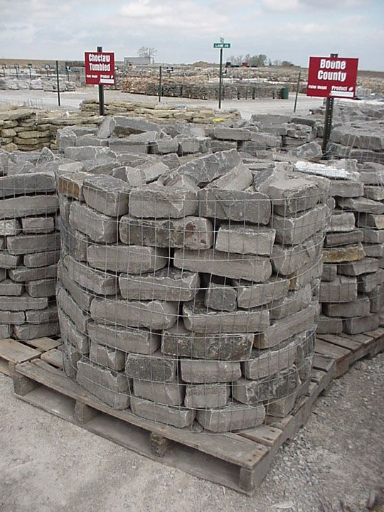 Pallets of gray rectangular stone blocks for landscaping, arranged in circular stacks at an outdoor masonry supply yard.