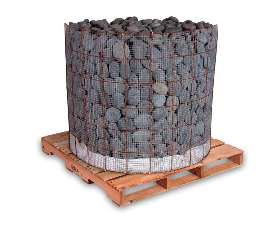 A cylindrical wire crate filled with smooth, dark grey river stones, sitting on a wooden shipping pallet.