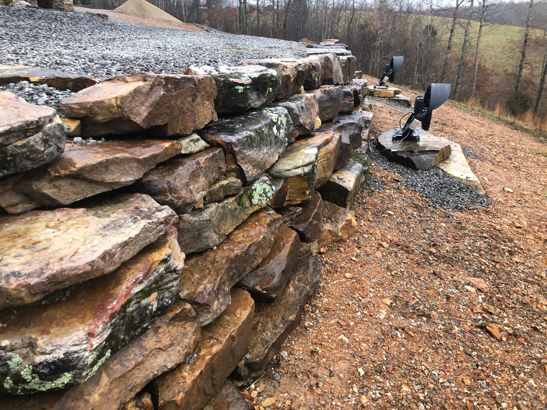 Stacked natural stone retaining wall beside a gravel path, with two landscape spotlights mounted on rocks.
