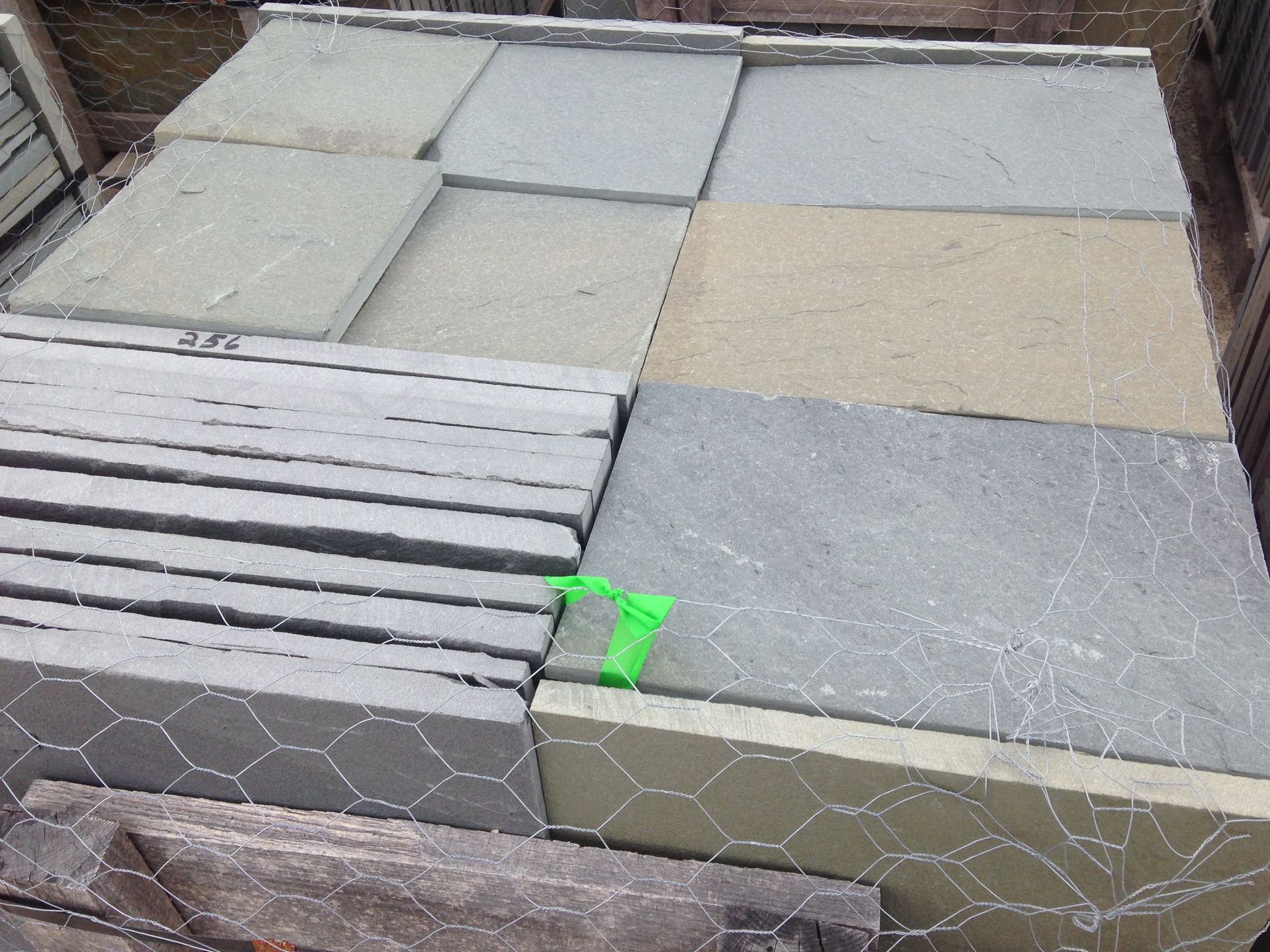 A stacked pallet of grey and tan stone paving slabs wrapped in wire fencing.