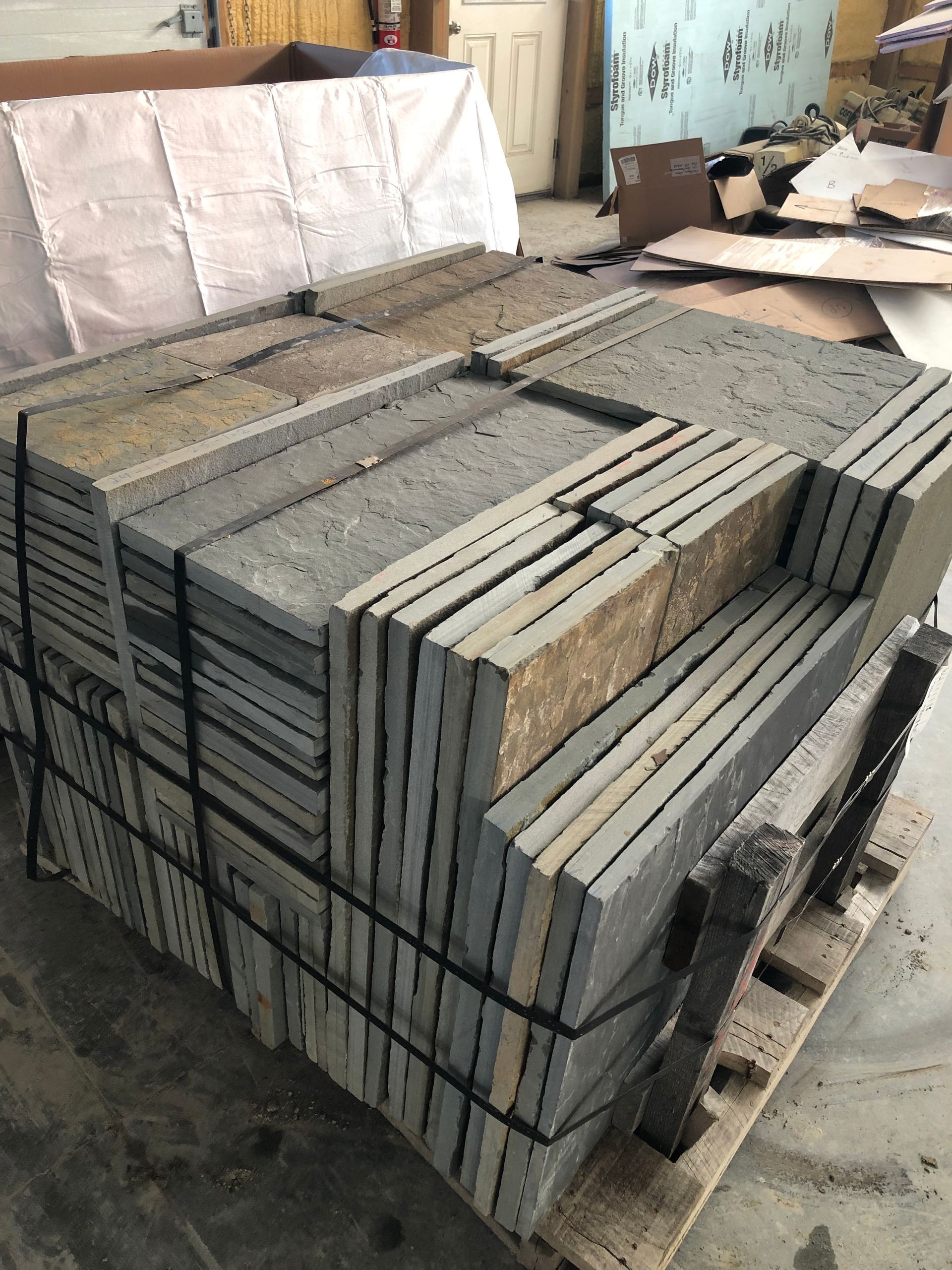 A wooden pallet loaded with stacked, rectangular grey stone pavers secured with black plastic strapping.