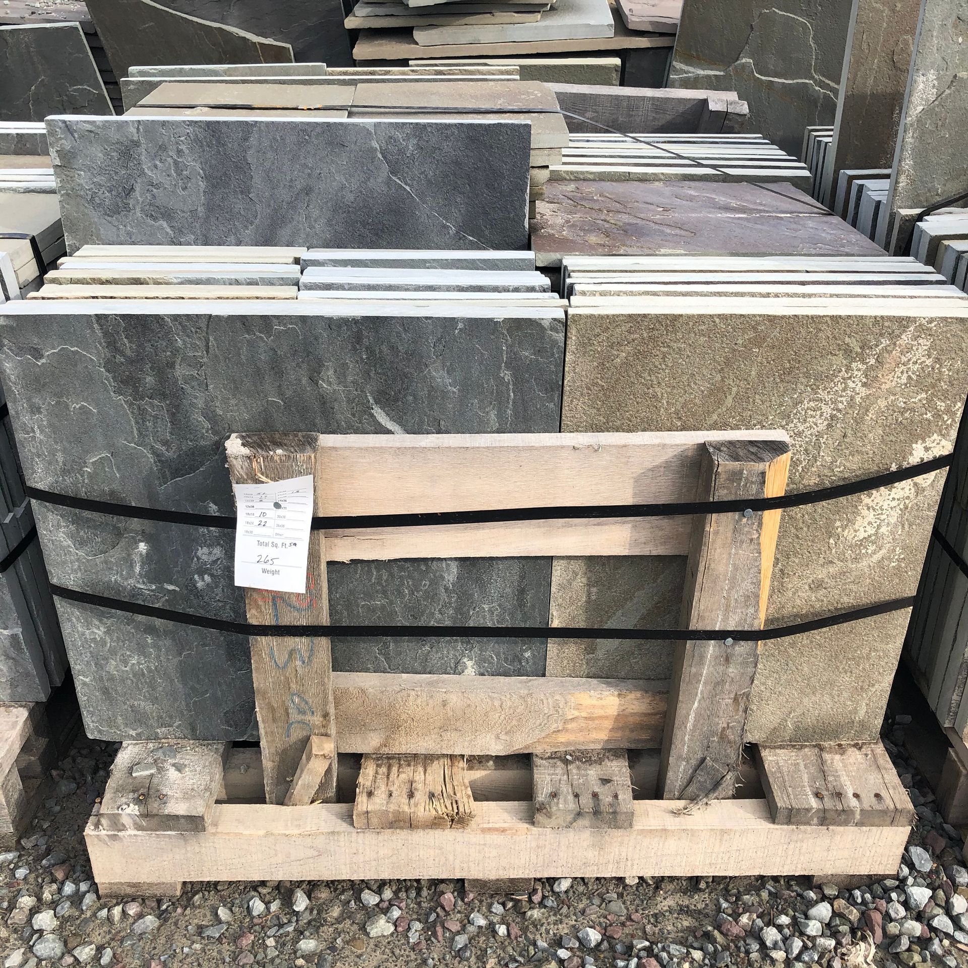 A wooden pallet holding a stack of square, multi-colored stone pavers in shades of gray, brown, and tan.