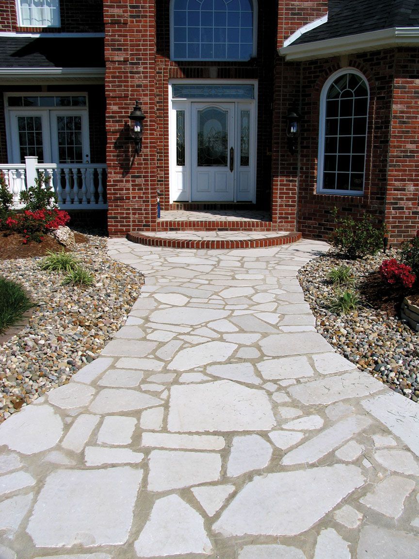 A light-colored stone path leads to the front entrance of a two-story brick house with white trim.