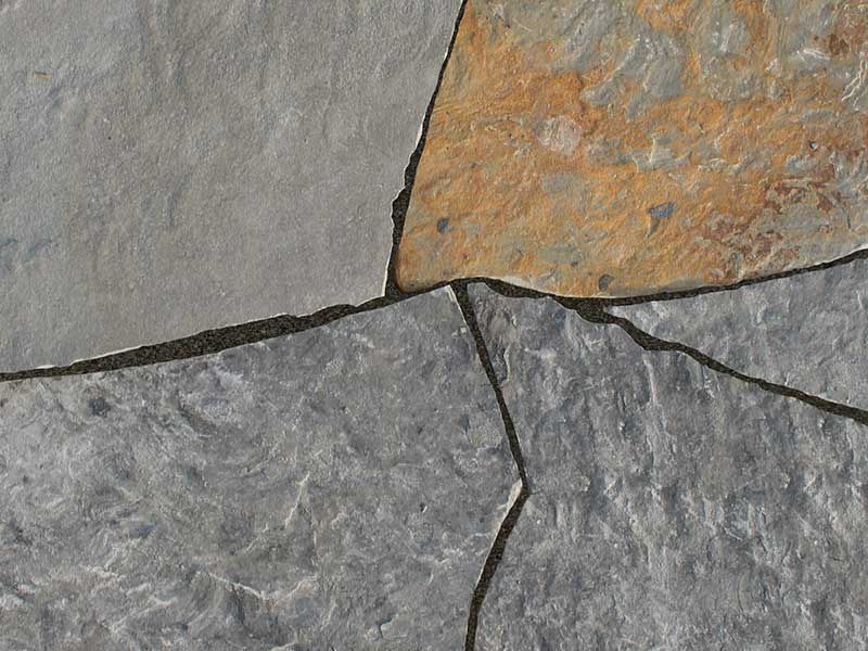 Close-up of irregular, textured natural stone paving slabs in shades of gray and rust brown.