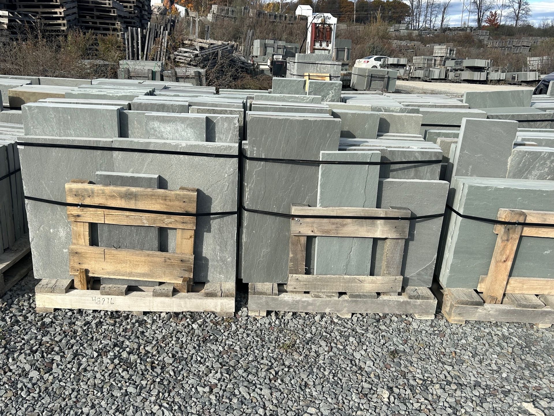 Stacks of gray stone slabs secured with black straps on wooden pallets in an outdoor supply yard.