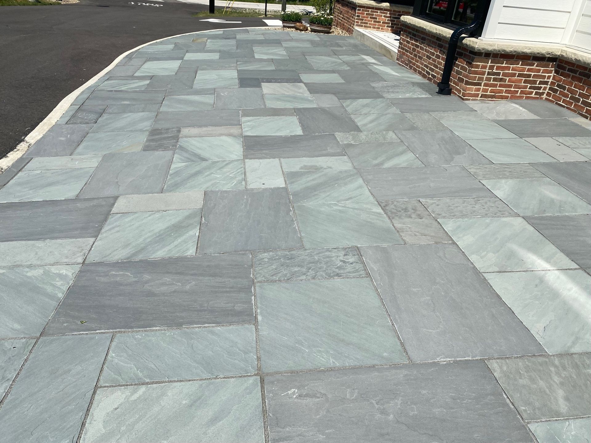 A paved walkway made of blue-gray rectangular stone slabs next to a brick foundation and an asphalt driveway.