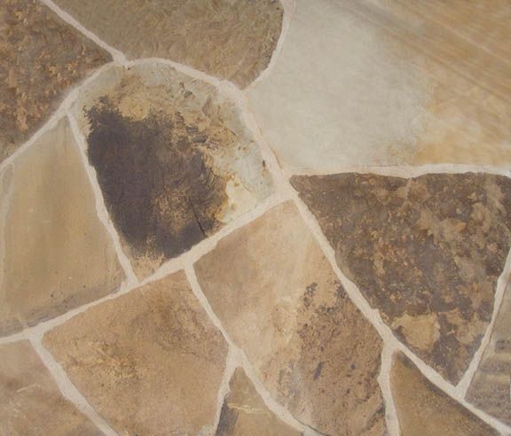 A close-up view of tan, brown, and gray flagstones with thick, off-white grout joints in an irregular pattern.